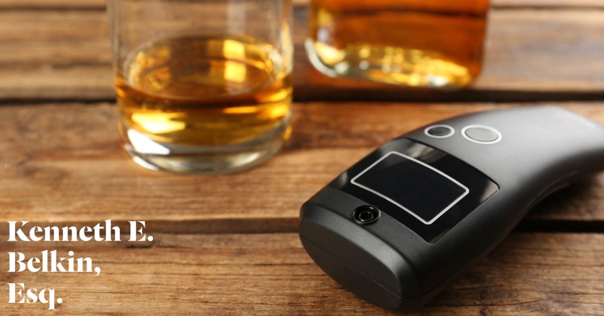 breathalyzer on wooden table next to dark liquor in glass and bottle